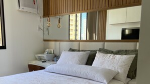 A bedroom with a large bed, a nightstand, a desk, a flat-screen TV, and a window with a view of buildings. - I rent an entire apartment in Aracaju. (Aracaju)