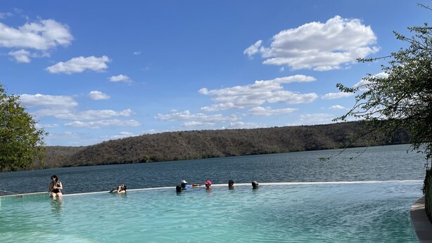 A clear swimming pool with a view of a lake and forested hills in the background. - I rent an entire apartment in Aracaju. (Aracaju)