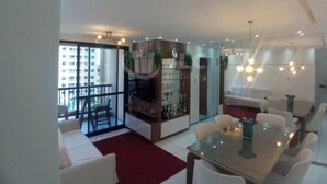 A modern living room with a glass dining table, white sofas, and a red rug. There is a balcony with a view of a building. - I rent an entire apartment in Aracaju. (Aracaju)