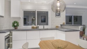 Una cocina moderna con armarios blancos, una mesa de comedor de madera y una lámpara colgante.