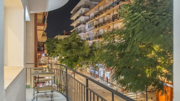 Un edificio de varios pisos con balcones, una calle peatonal y árboles.