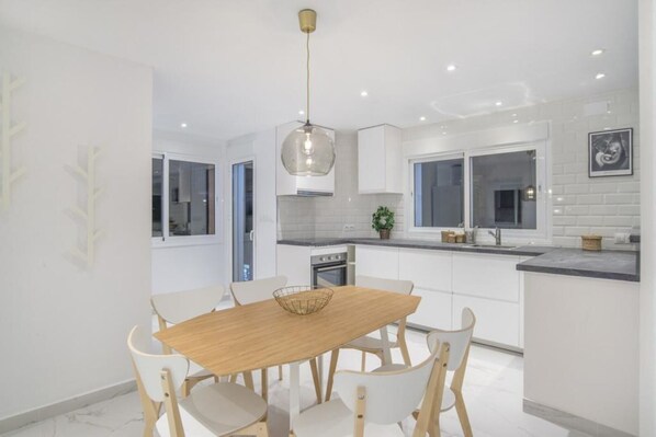 Une cuisine moderne avec des meubles blancs, une table à manger en bois et un luminaire suspendu.