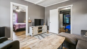 A modern living room with a wooden coffee table, grey sofas, a TV, and a bed in the adjacent room. - Rustic Home w/ 2 BR - WIFI included (Louisville)