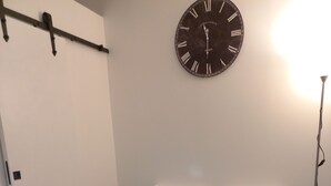 Un dormitorio con cama, dos almohadas, un reloj de pared y una puerta.