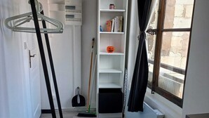 Una habitación con suelo de madera, un radiador blanco, una estantería, una escoba y un tendedero.