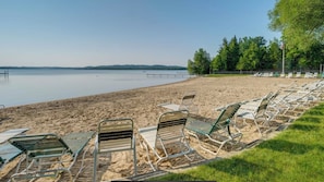 A beach with metal lounge chairs and a calm lake.