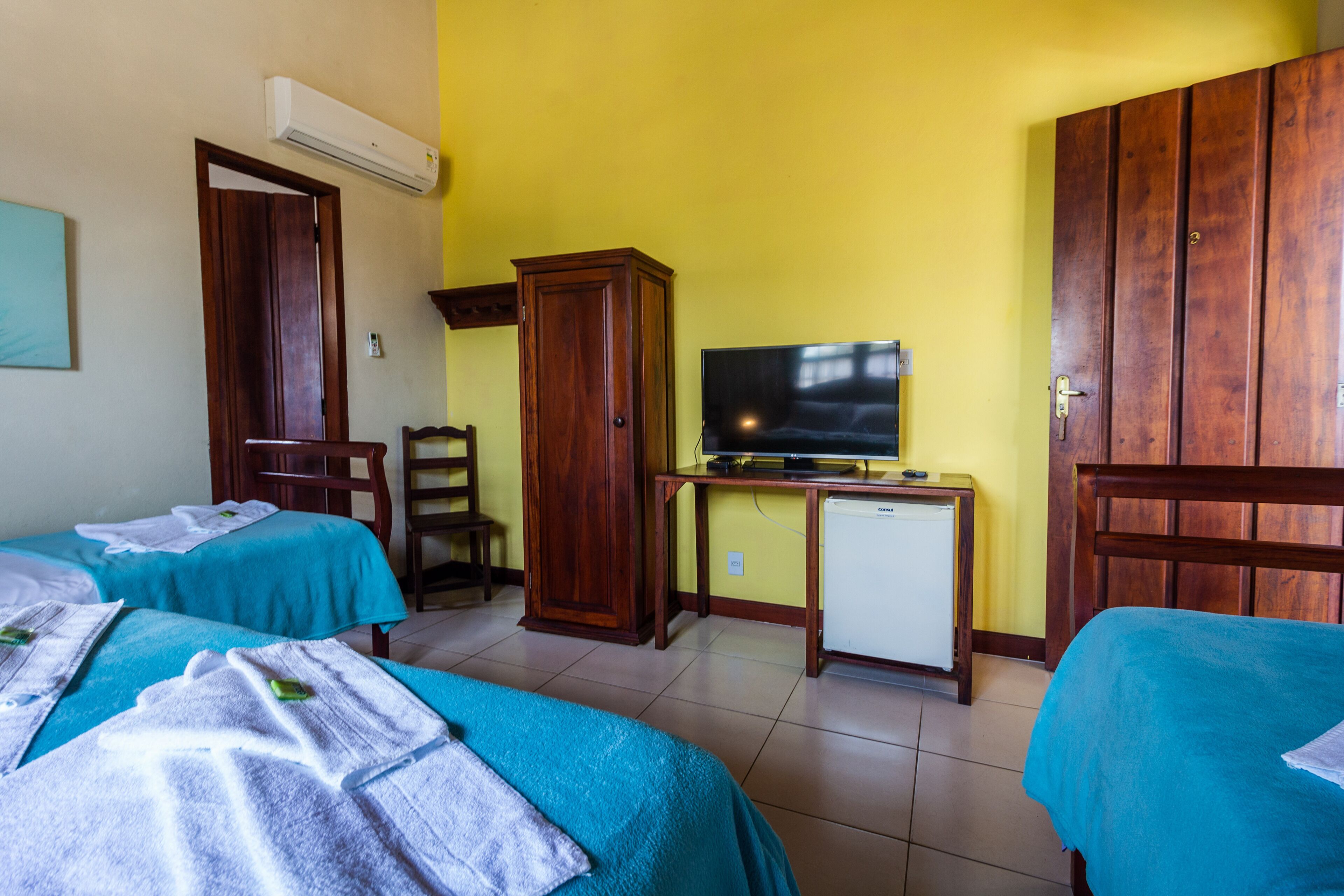 A hotel room with two beds, a television, a small refrigerator, and wooden furniture.