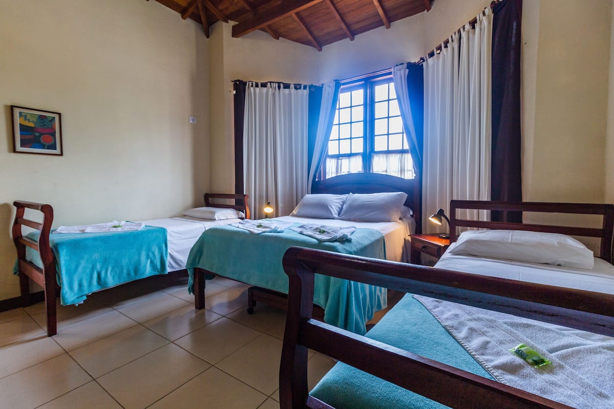A hotel room with two single beds, a wooden chair, a small table, and a window with curtains.