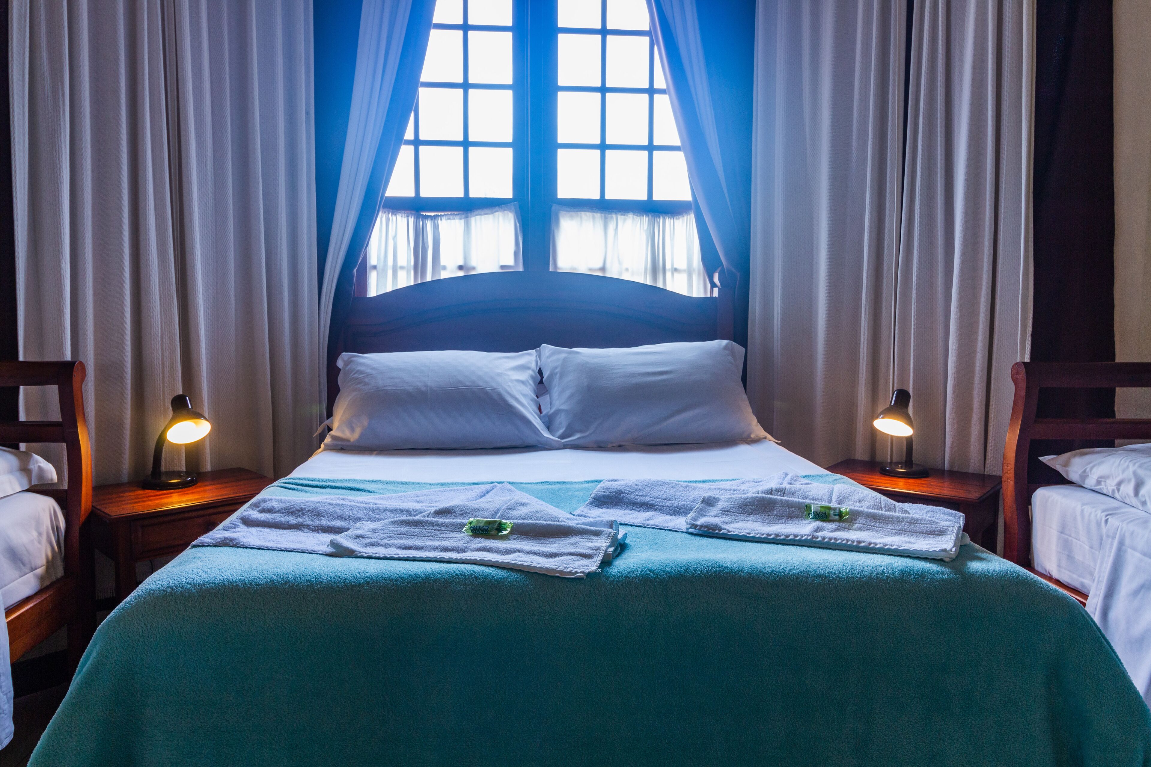 A neatly made bed with white linens, two bedside lamps, and a window with curtains.