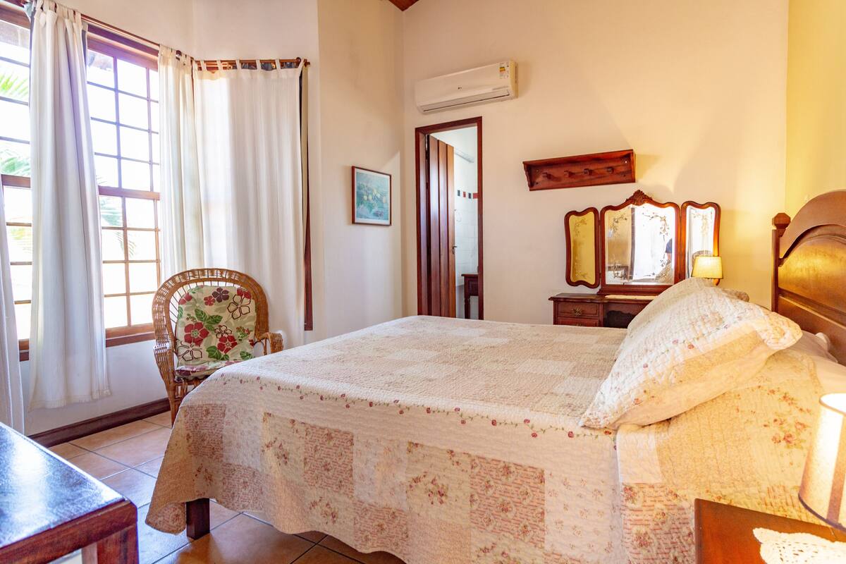 A bedroom with a bed, a chair, a table, and a window with curtains.