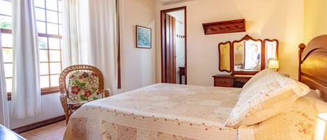Quarto com cama, cadeira, mesa e janela com cortinas.