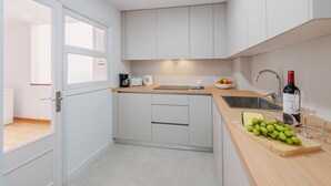 Una cucina moderna con mobili bianchi, un piano di lavoro in legno, un lavello e un tagliere con grappoli d'uva.