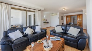 Un soggiorno con due divani in pelle nera, un tavolino in legno e, sullo sfondo, una zona pranzo.