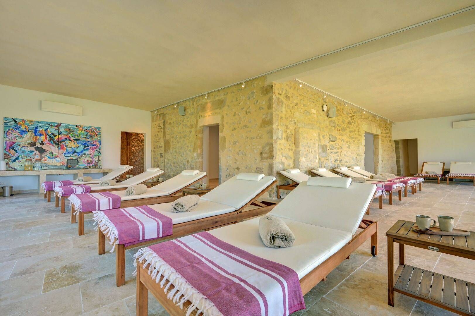 Un área de spa con varias tumbonas, paredes de piedra y una obra de arte grande en la pared.