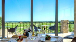 A dining table set with plates, glasses, and a bottle, overlooking a scenic landscape with a stone pillar and a metal fence. - Domaine de Privadière & Spa (Garrigues-Sainte-Eulalie)