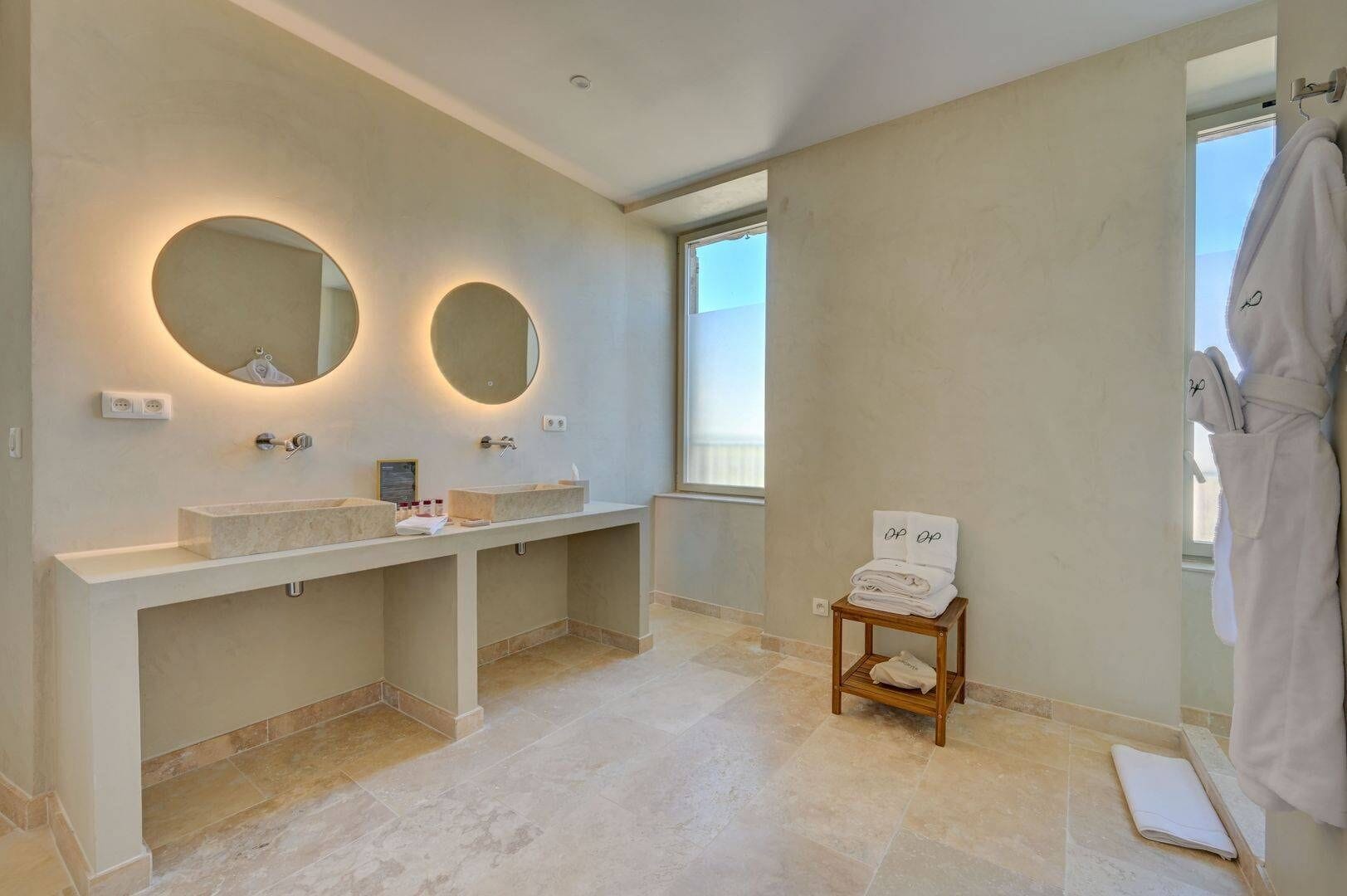 Un baño moderno con dos lavamanos, un mueble de tocador y un pequeño taburete de madera con toallas.