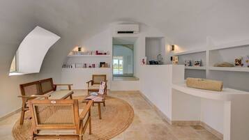 Ein geräumiges Loft mit hohen Decken, einem Oberlicht, einer eingebauten Bücherwand und einer gemütlichen Sitzecke mit Holzmöbeln und einem gewebten Teppich.