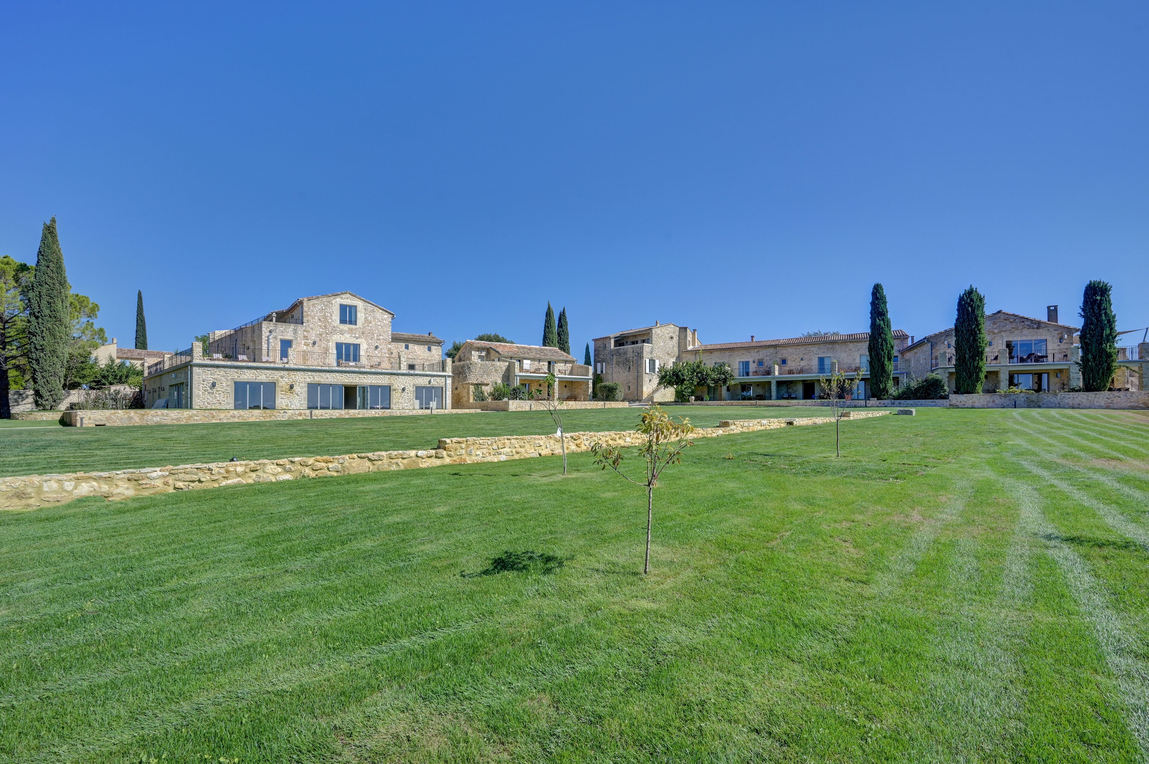 A stone building with multiple rooms, a large lawn, and tall trees.