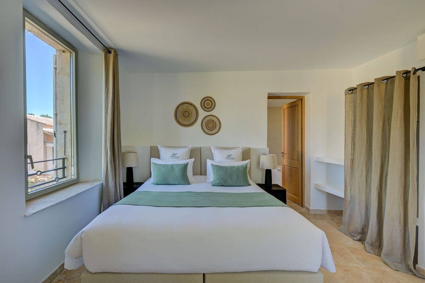 Habitación de hotel con una cama grande, una ventana con cortinas, una puerta y decoración en las paredes.