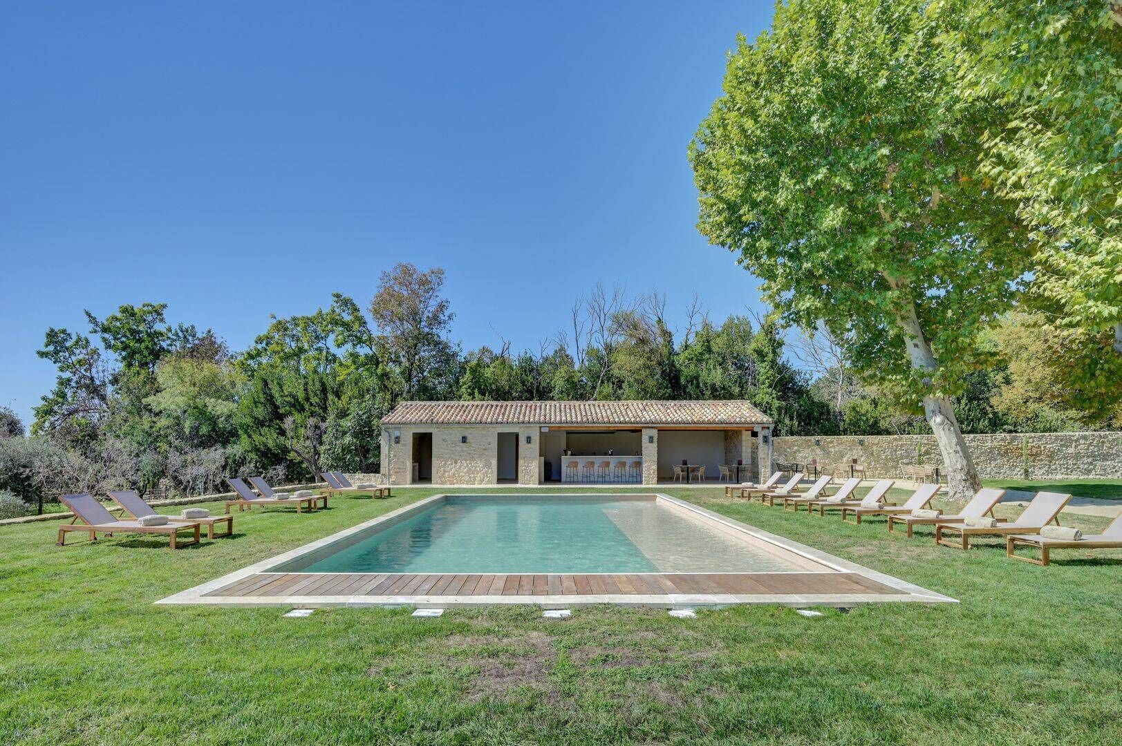 A poolside area with a stone building, lounge chairs, and a clear blue sky.