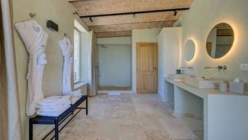 A modern bathroom with a bench holding towels, a wooden door, and a vanity with a mirror.