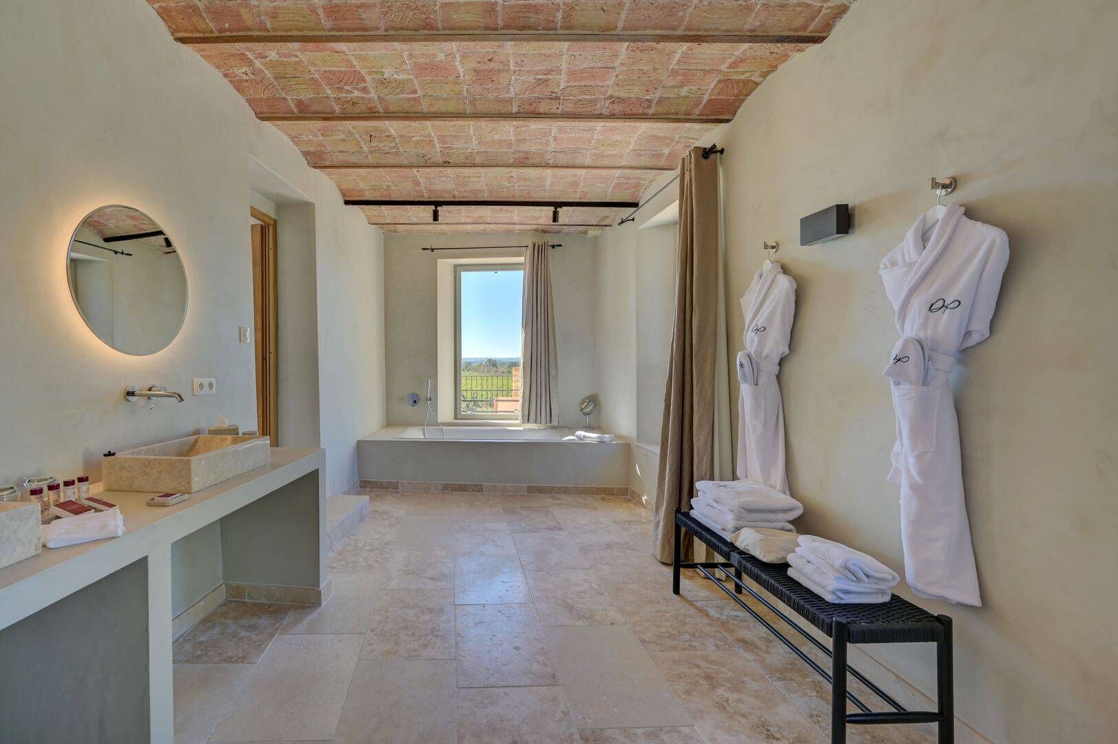 Une salle de bain avec une baignoire, un grand miroir et un meuble-lavabo. Des serviettes et des peignoirs sont suspendus sur un porte-serviettes.