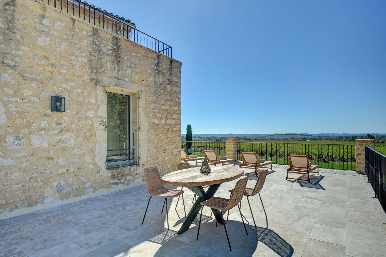 Un bâtiment en pierre doté d’un balcon, avec une table ronde et des chaises, une porte et une vue sur les vignes.