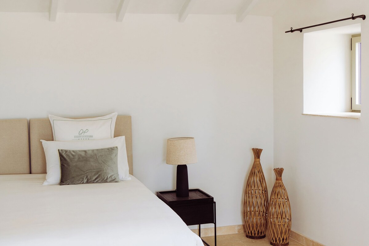 A bedroom with a bed, bedside table, lamp, and decorative vases.