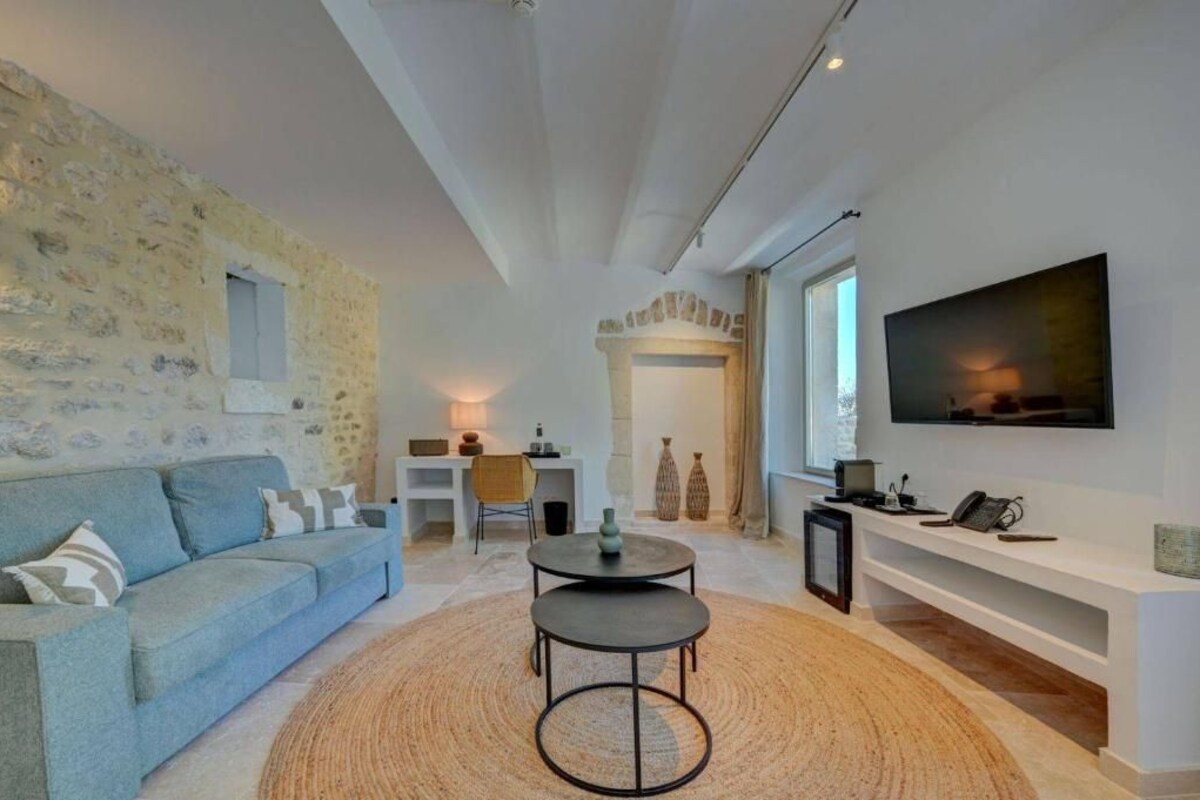 A modern living room with a stone wall, a sofa, a round coffee table, a TV, and a fireplace.