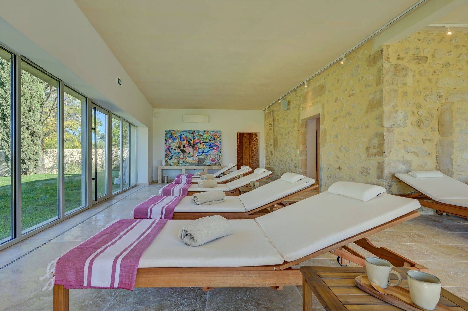 A spa room with multiple sunbeds, a large window, and a stone wall.