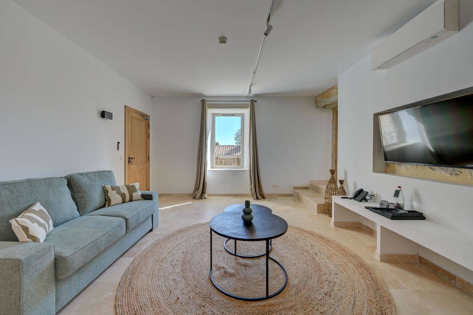 Ein modernes Wohnzimmer mit einer Couch, einem Couchtisch, einem Fernseher und einem Fenster mit Vorhängen.