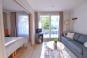 A modern hotel room with a bed, a sofa, a TV, and a balcony with curtains. - Cosy Apt With Balcony - Buttes Chaumont (Paris)