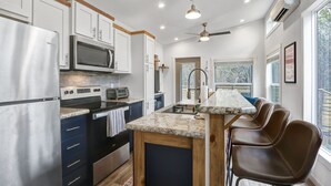 A modern kitchen with white cabinets, stainless steel appliances, a marble countertop, and a bar area with brown chairs.