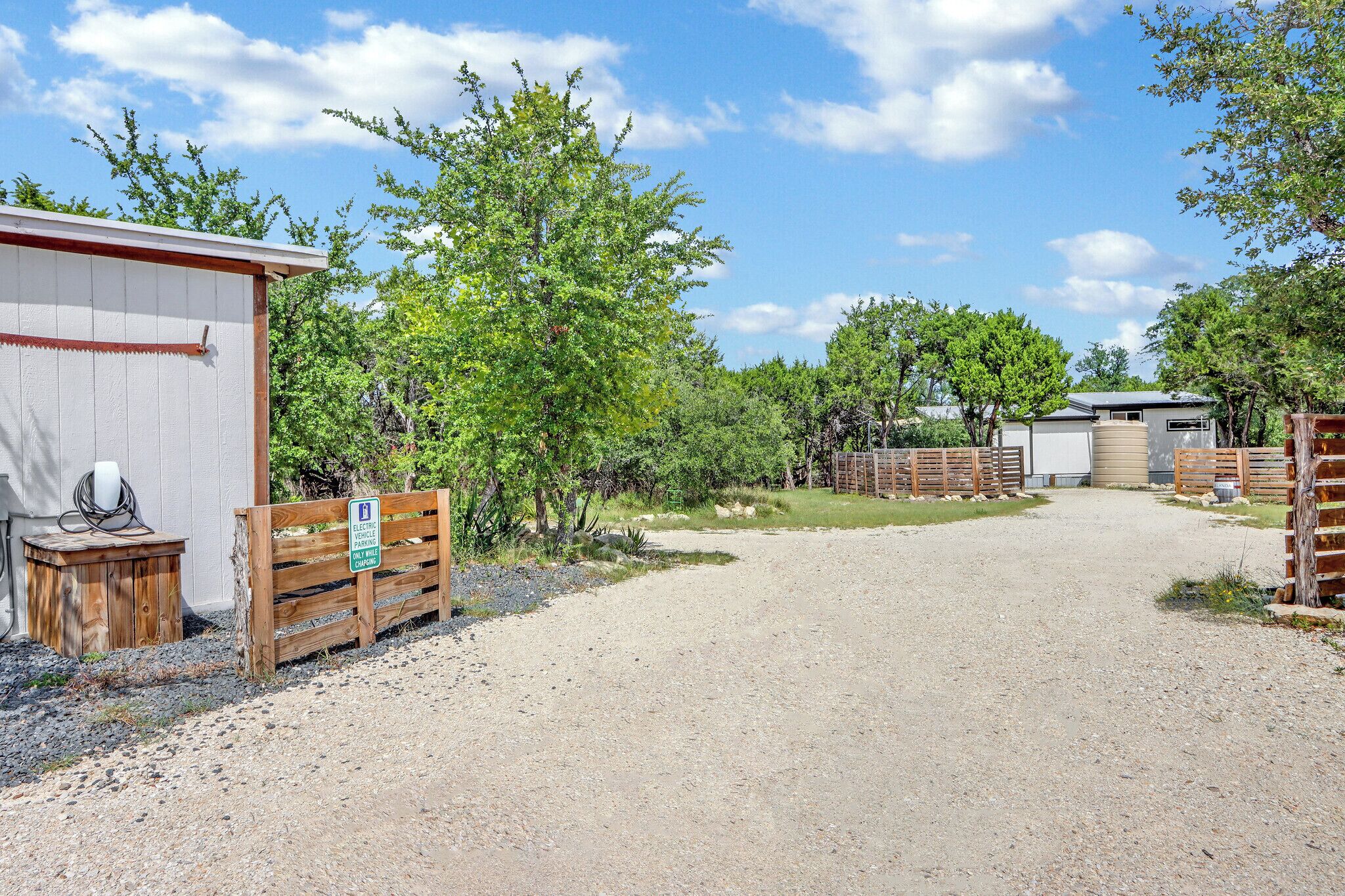 A gravel driveway leading to a building with a wooden fence and a sign indicating electric vehicle charging.
