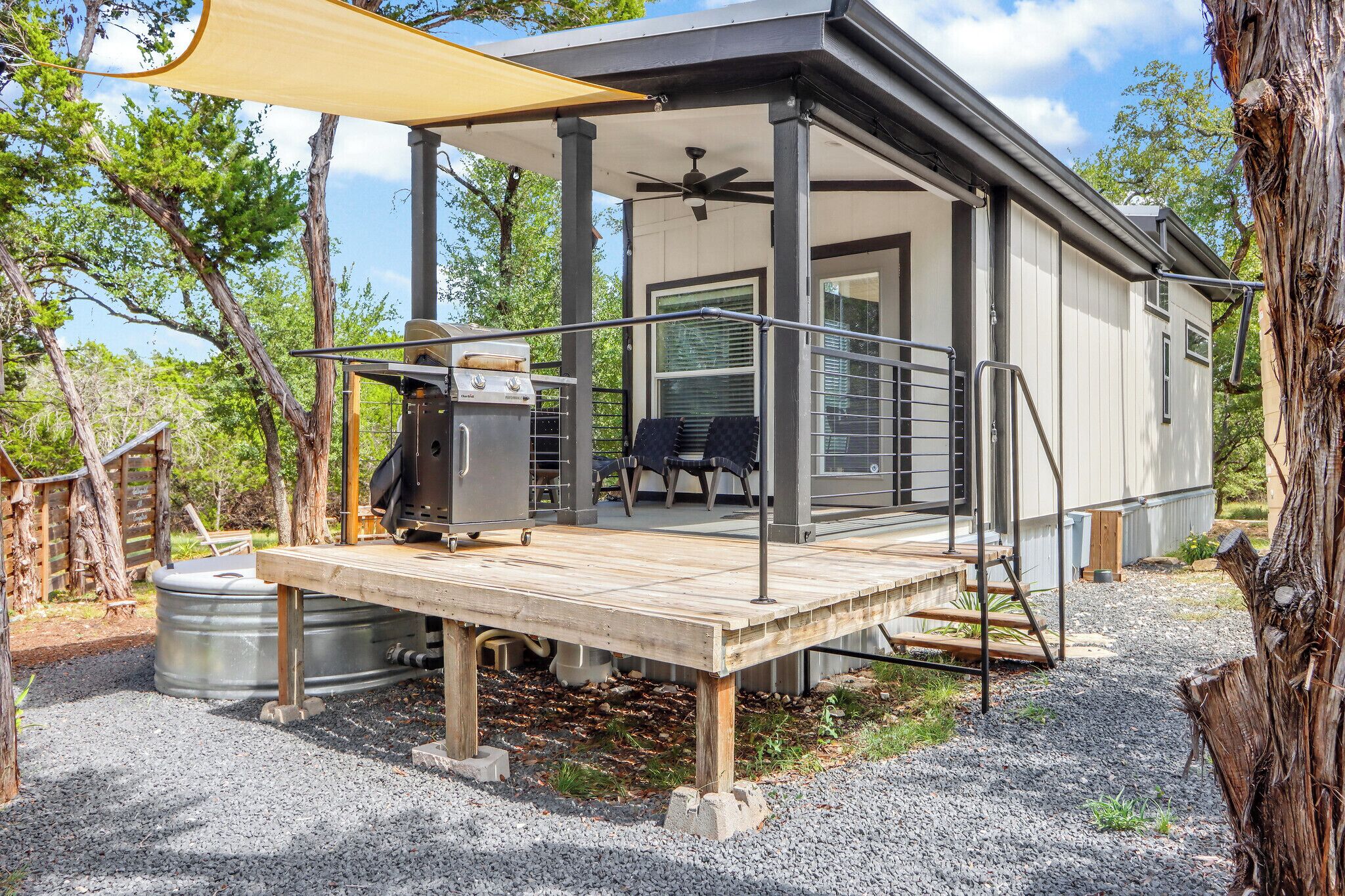 Een moderne camper met een overdekt terras, een barbecue en een groot raam.