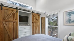 A bedroom with a bed, a TV, wooden sliding doors, and a window with a view of trees.