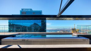 En takpool som ser ut att gå över kanten och smälta samman med horisonten, med utsikt över staden, modern arkitektur och en klar himmel.