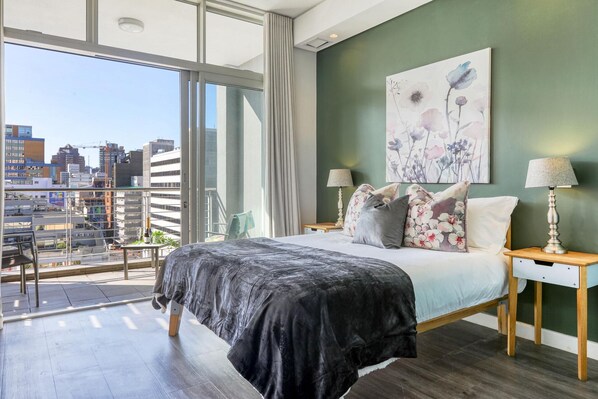 A modern bedroom with a large bed, two bedside tables, a city view balcony, and a green accent wall.