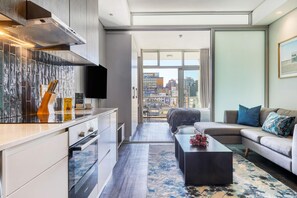 A modern living room with a sofa, coffee table, and a view of the cityscape through large windows.