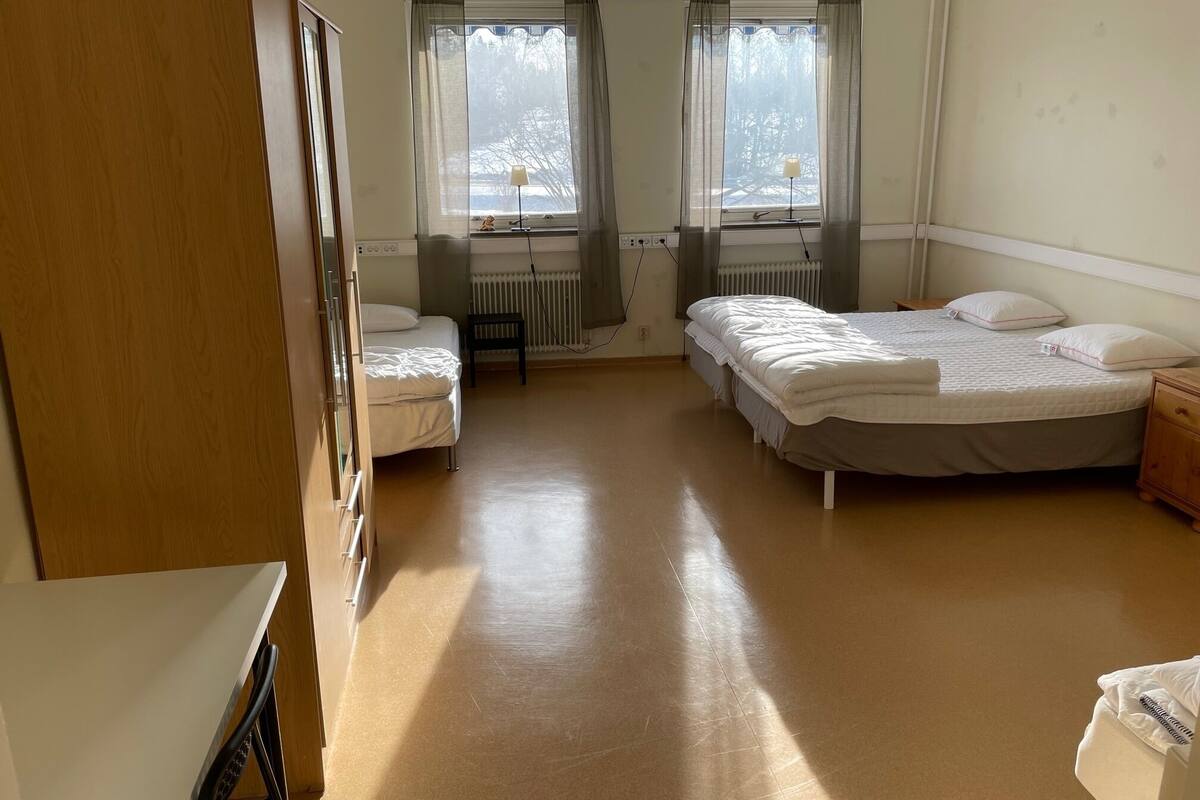 Ein Hotelzimmer mit zwei Betten, einem Holzschrank, einem Schreibtisch und einer Heizung.