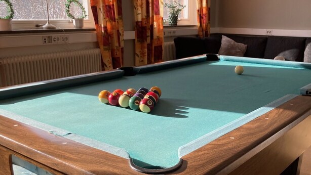 Una mesa de billar con bolas, una ventana con cortinas y un radiador.