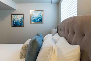 Un dormitorio con una cama grande, dos cuadros colgados en la pared y una ventana con persianas.