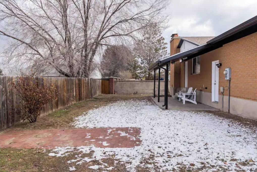 Un jardin avec une terrasse en briques, une clôture en bois et un espace de détente couvert équipé de chaises.