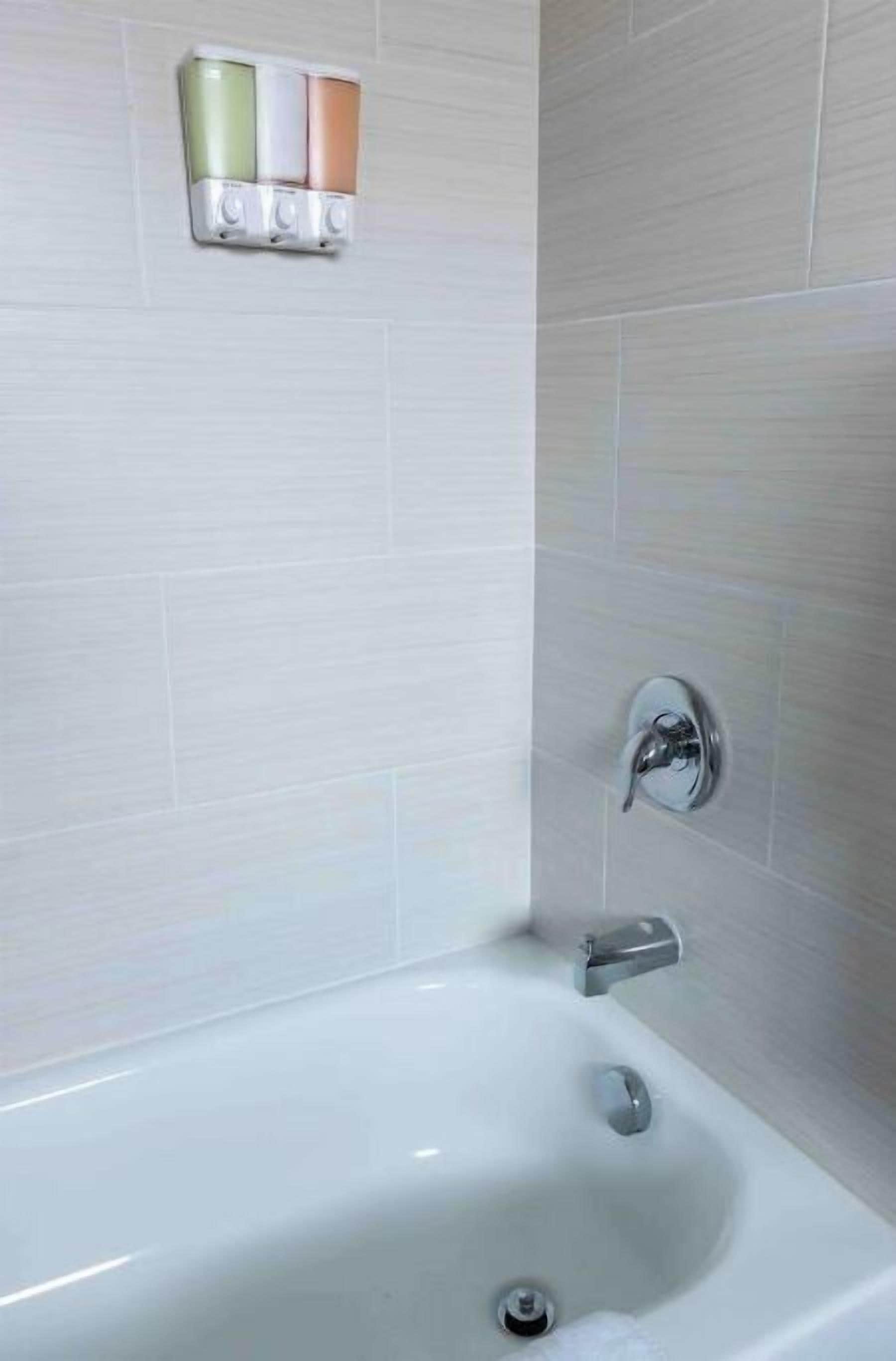 A bathroom with a white bathtub, a chrome faucet, and a wall-mounted soap dispenser with three colors.
