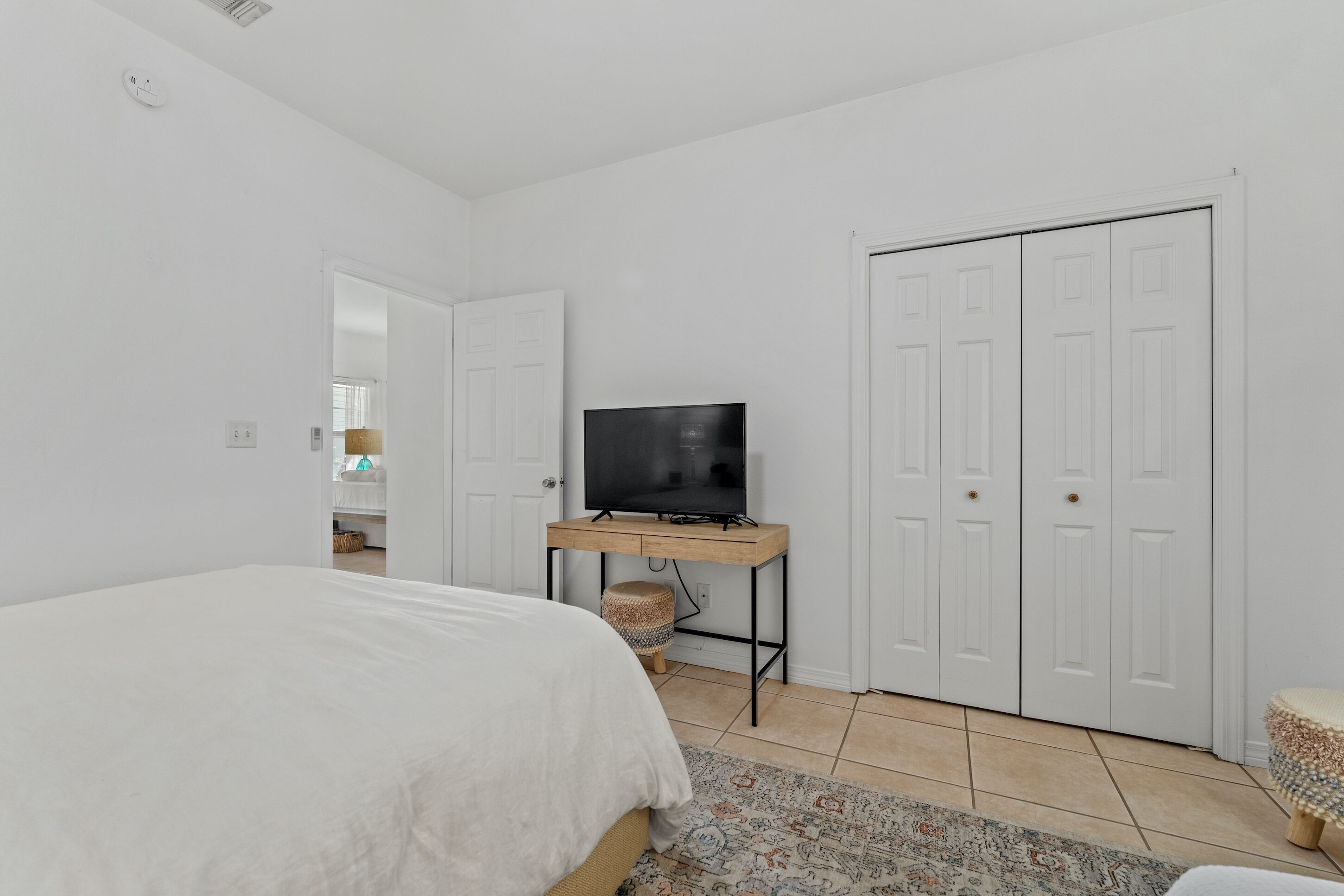 A bedroom with a bed, a TV on a wooden stand, a wardrobe, and a patterned rug.