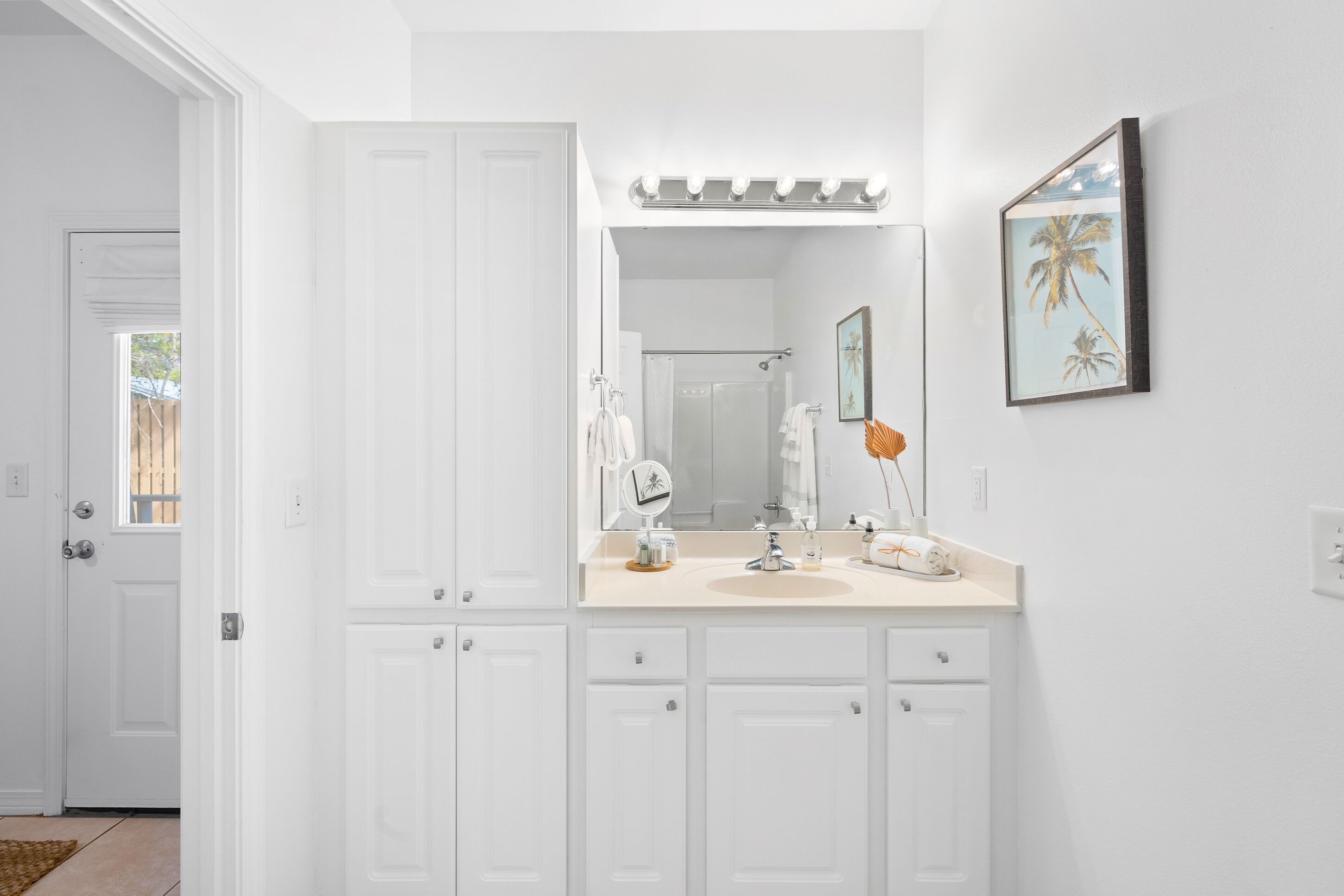 Un baño con muebles blancos, un tocador con espejo y un cuadro en la pared.