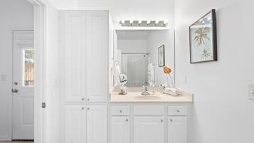 Un baño con muebles blancos, un tocador con espejo y un cuadro en la pared.