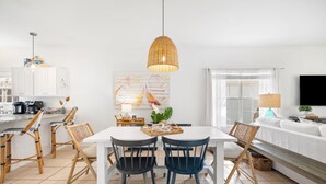 A modern kitchen with white cabinets, a dining table with chairs, and a hanging light fixture.
