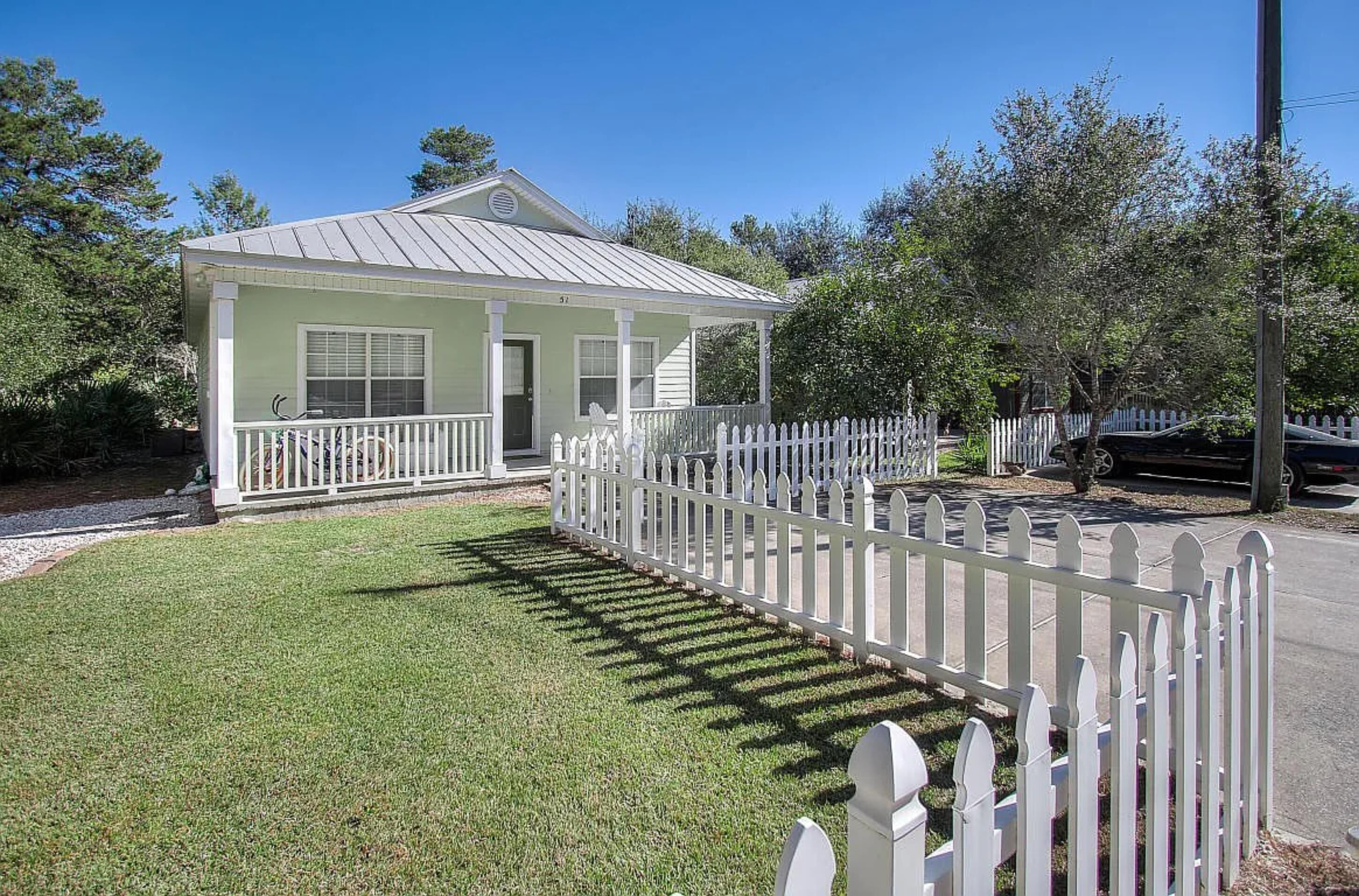 A small, single-story house with a white picket fence and a covered porch.