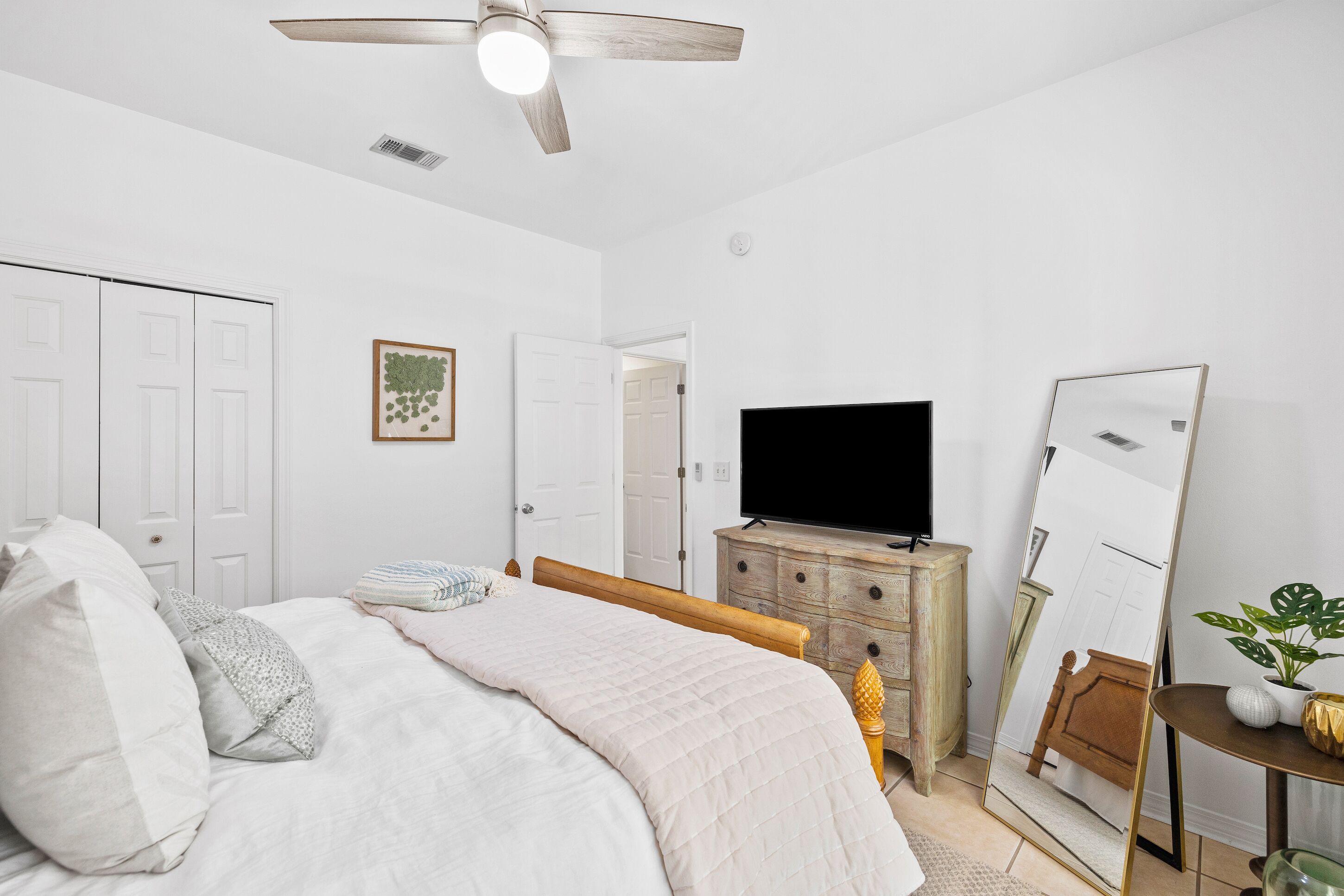 Ein Schlafzimmer mit Bett, Schminktisch, Fernseher, Spiegel und Deckenventilator.